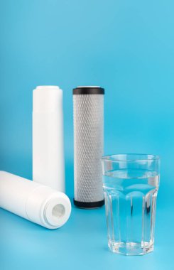 set three of cartridges for water filter with clear glass of water isolated on blue background.  Concept of water treatment technology. filter cartridges to domestic water treatment systems 