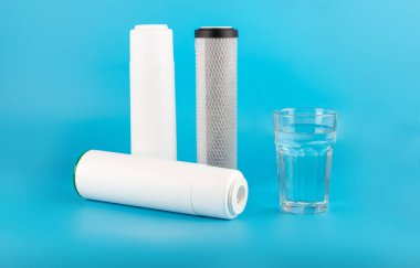 set three of cartridges for water filter with clear glass of water isolated on blue background.  Concept of water treatment technology. filter cartridges to domestic water treatment systems 