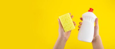 Cleaning yellow sponge and detergent for dishes holding in hand on a yellow background. Top view, flatlay, close up. Concept cleaning company, purity, cleaning, kitchen