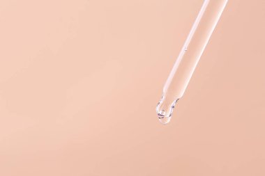 Transparent essential serum oil dripping from gold dropper isolated on beige background. Clipping path.
