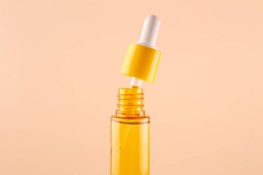 glass yellow bottle with pipette with essential oil on beige background top view. Aromatic cosmetic product for skin hair care Moisturizing beauty product with vitamin C close up