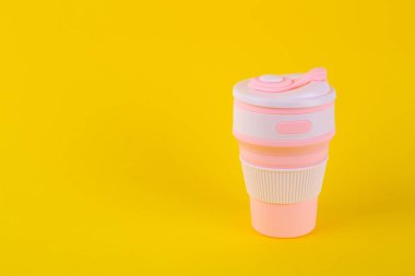 reusable pink silicone cup. folding cup isolated on yellow background. replacement of plastic cup