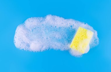 Cleaning yellow sponge and a soapy bubble foam on a blue background. Cleaning concept, cleaning service. Banner. Flat lay, top view