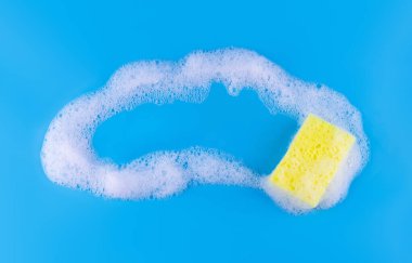 Cleaning yellow sponge and a soapy foam with copyspace inside on a blue background. Cleaning concept, cleaning service. Banner. Flat lay, top view