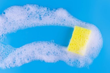 Cleaning yellow sponge and a soapy foam with copyspace inside on a blue background. Cleaning concept, cleaning service. Banner. Flat lay, top view