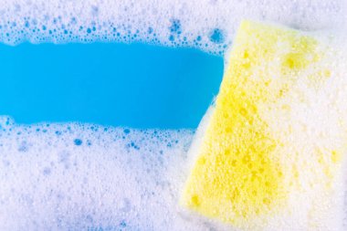 Cleaning yellow sponge and a soapy bubble foam on a blue background. Cleaning concept, cleaning service. Banner. Flat lay, top view