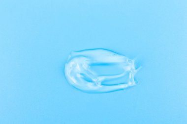Smear of cosmetology transparent product for face treatment. Drop of cream on blue background. Lotion or mask. Beauty wellness and professional skincare concept.