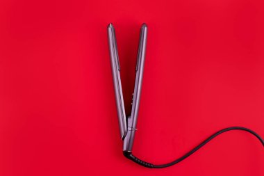 Modern hair iron for straightening on red background, top view with space for text