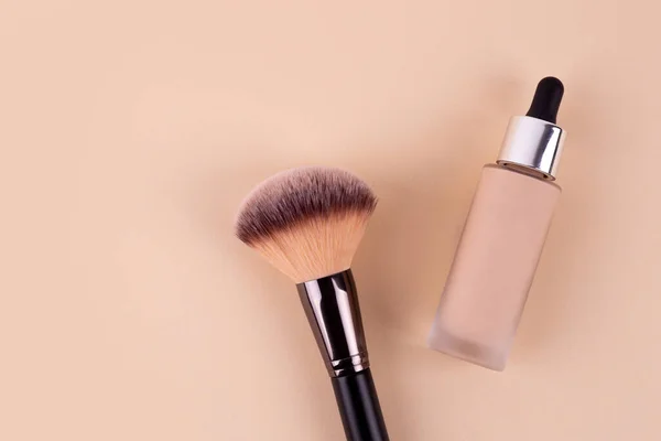 Liquid foundation cream unbranded bottle with makeup brush. Facial correction, liquid concealer, tone, bb, cc cream skincare product on beige background. Feminine cosmetics accessory with copy space