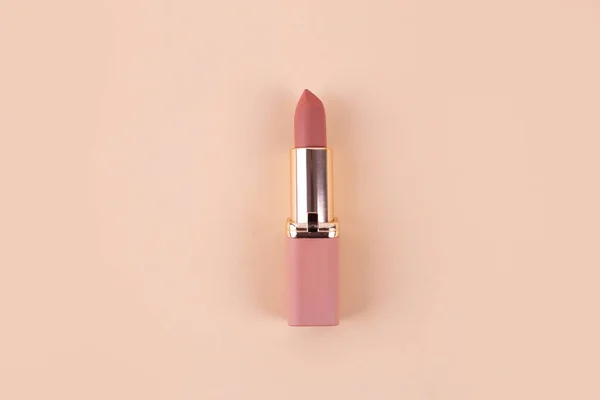 nude matte lipstick on a beige background in a pink and gold tube top view, flatlay. Professional cosmetic product for the work of a makeup artist flat lay. Bright backdrop vertical