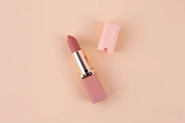 nude matte lipstick and cap on a beige background in a pink and gold tube top view. Professional cosmetic product for the work of a makeup artist flat lay. Bright backdrop horizontal