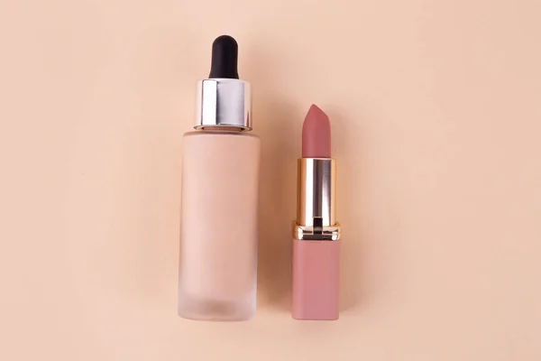 Liquid foundation cream unbranded bottle and nude lipstick on a beige background. BB cream for professional make-up, eyedropper for applying to the face. Cosmetic female accessory. Mock up concept