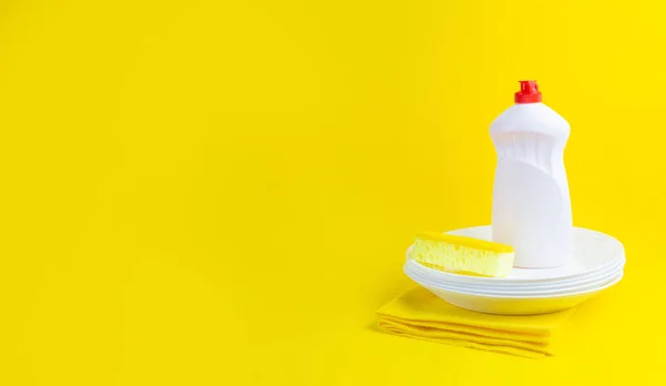 Cleaning yellow sponge, white plate and detergent for dishes on a yellow background. Top view, close up. Concept cleaning company, purity, cleaning, kitchen