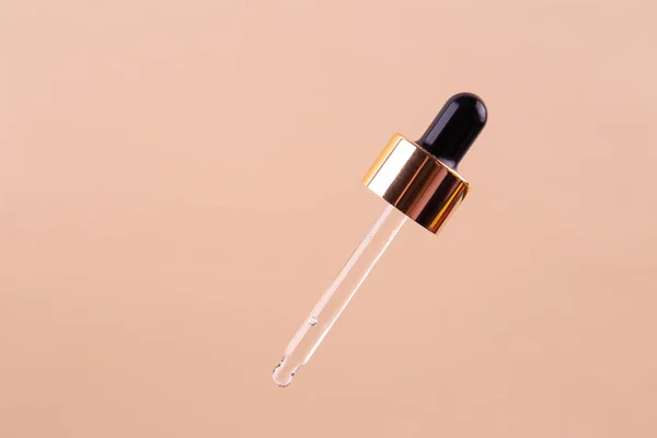 Transparent essential serum oil dripping from gold dropper isolated on beige background. Clipping path