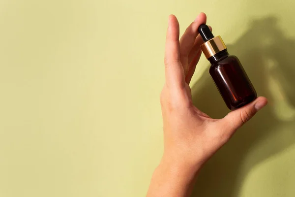 Serum bottle in female hands, top view. Transparent moisturizer for skin care. Nourishing essential oil in glass bottle with pipette. Liquid emulsion with hyaluronic acid. Beauty cosmetic spa product