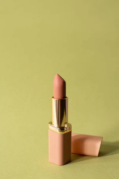 Nude matte lipstick with a cap on a pastel green background. Female accessory for lip makeup. Professional cosmetic product for makeup artists in the composition. Backdrop