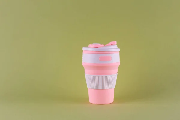 reusable pink silicone cup. folding cup isolated on pastel green background. replacement of plastic cu