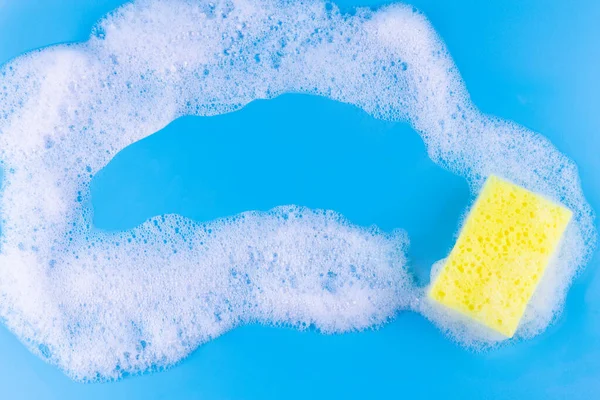 Cleaning yellow sponge and a soapy foam with copyspace inside on a blue background. Cleaning concept, cleaning service. Banner. Flat lay, top view