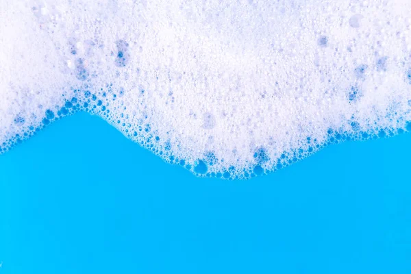 Foaming liquid on blue backdrop. Cosmetics foam background. Cosmetic product sample of mousse, shampoo or soap. Skincare, cosmetology and beauty concept