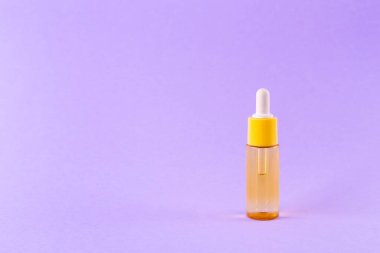 glass yellow bottle with pipette with essential oil on purple background top view. Aromatic cosmetic product for skin hair care Moisturizing beauty product with vitamin C close up