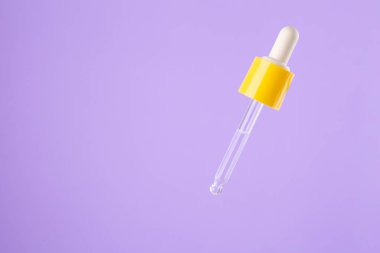 Essential clear oil or serum in pipette isolated on pastel purple background close up. cosmetic pipette