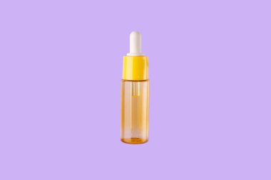 glass yellow bottle with pipette with essential oil on purple background top view. Aromatic cosmetic product for skin hair care Moisturizing beauty product with vitamin C close up