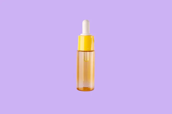glass yellow bottle with pipette with essential oil on purple background top view. Aromatic cosmetic product for skin hair care Moisturizing beauty product with vitamin C close up