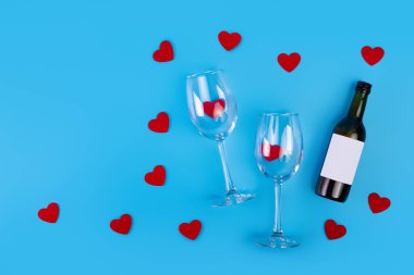 Top view photo of romantic evening, dinner decor hearts love wineglasses with confetti wine bottle on isolated blue background with copyspace