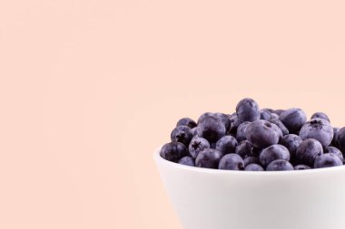 Beautiful fresh blueberries in a white bowl on a beige background with copyspace. Vegan and vegetarian concept. Summer healthy food. 