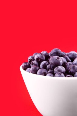 Beautiful fresh blueberries in a white bowl on a red backgroun
