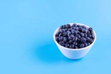 Fresh blueberries in white plate on blue background. Vegan and vegetarian concept. Summer healthy food. Flatla