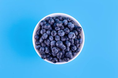Fresh blueberries in white plate on blue background. Vegan and vegetarian concept. Summer healthy food. Flatla