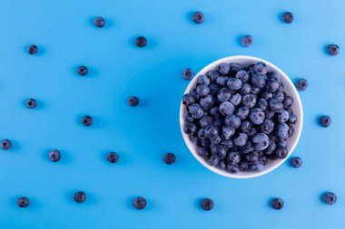 Fresh blueberries in white bowl on blue background. Flat lay, top view