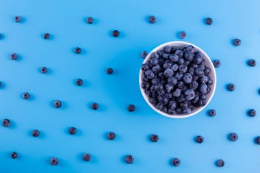 Fresh blueberries in white bowl on blue background. Flat lay, top view
