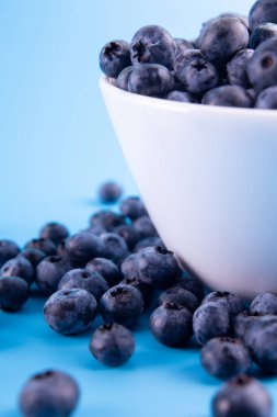 Blueberries on a macro scale. Dark berries in bowl close-up. Ripe blueberries isolated on blue background. Healthy, natural fruit