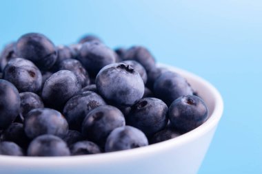 Blueberries on a macro scale. Dark berries in bowl close-up. Ripe blueberries isolated on blue background. Healthy, natural fruit
