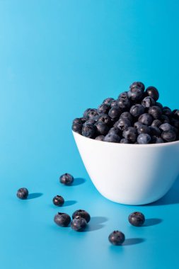 Beautiful fresh blueberries in a white bowl on a blue backgroun