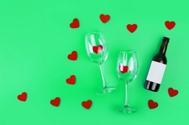 Top view photo of romantic evening, dinner decor hearts love wineglasses with confetti wine bottle on isolated green background with copyspace