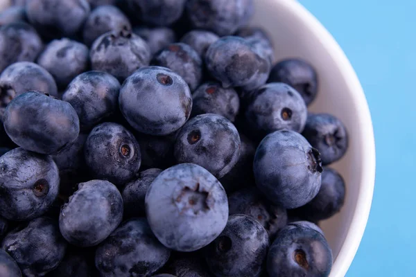 Blueberries on a macro scale. Dark berries in bowl close-up. Ripe blueberries isolated on blue background. Healthy, natural fruit