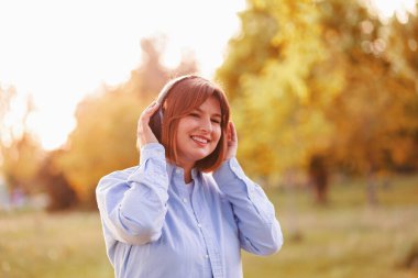 Young smiling woman listening music with headphones at sunset. Caucasian girl listening songs via wireless black headphones. Closeup face of teen and keeps the rhythm of the song.
