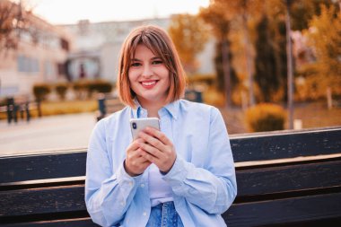Photo of charming pretty young lady communicating modern gadget sitting bench smiling outside urban city street