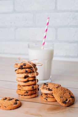 Composition of freshly baked homemade biscuits with chocolate chips. Healthy breakfast concept with glass of milk and cooked cookies on wooden table for overlay on product presentation