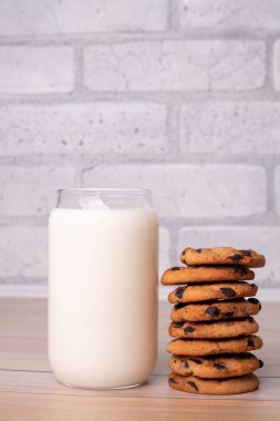 Composition of freshly baked homemade biscuits with chocolate chips. Healthy breakfast concept with glass of milk and cooked cookies on wooden table for overlay on product presentation.