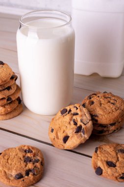 Flatlay an after school snack of chocolate chip cookies and an glass cup of milk, bottle of milk. The cookies with chocolate drops and on a rustic wood kitchen table, with copy space. yummy and tasty