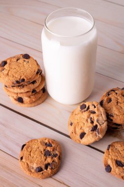 Flatlay an after school snack of chocolate chip cookies and an glass cup of milk. The cookies with chocolate drops and on a rustic wood kitchen table, with copy space. yummy and tasty
