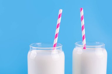 Milk glass cups with retro striped straws on isolated blue background. 