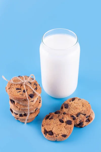 Glass of fresh milk and brown school chocolate cookies on blue background. Sweet food yummy and tasty concept. Flatlay an after school snack of chocolate chip cookies.