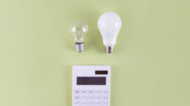 Beyaz hesap makinesi ve parlak lamba ya da zeytin zemininde LED ampul. Elektrik faturalarının ödenmesi kavramı. Tasarruf elektriği kavramı. Faturaların ödenmesinde indirim