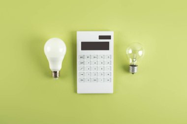 Beyaz hesap makinesi ve parlak lamba ya da zeytin zemininde LED ampul. Elektrik faturalarının ödenmesi kavramı. Tasarruf elektriği kavramı. Faturaların ödenmesinde indirim