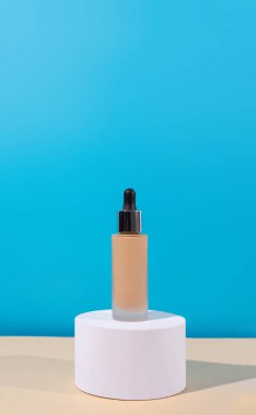 Temelde sıvı bej krem olan bir şişe, beyaz podyum. Mükemmel cilt için profesyonel makyaj ürünü. Kadın aksesuarları, temel güzellik ürünleri, astar, kapatıcı..